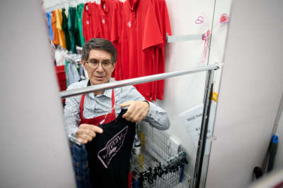 thrift store employee smiles as he hangs a t-shirt